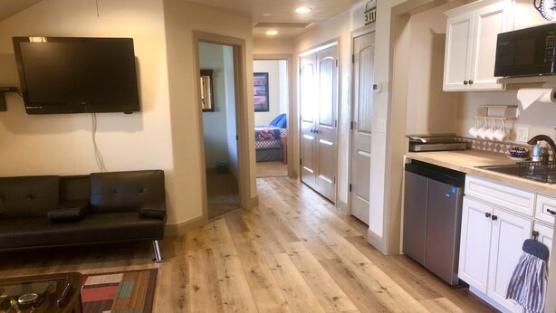 Uma sala de estar moderna com um sofá preto, uma televisão de tela plana e piso de madeira.