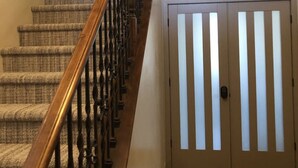 Uma escada com corrimão de madeira e degraus carpetados, conduzindo a uma porta com ripas verticais.