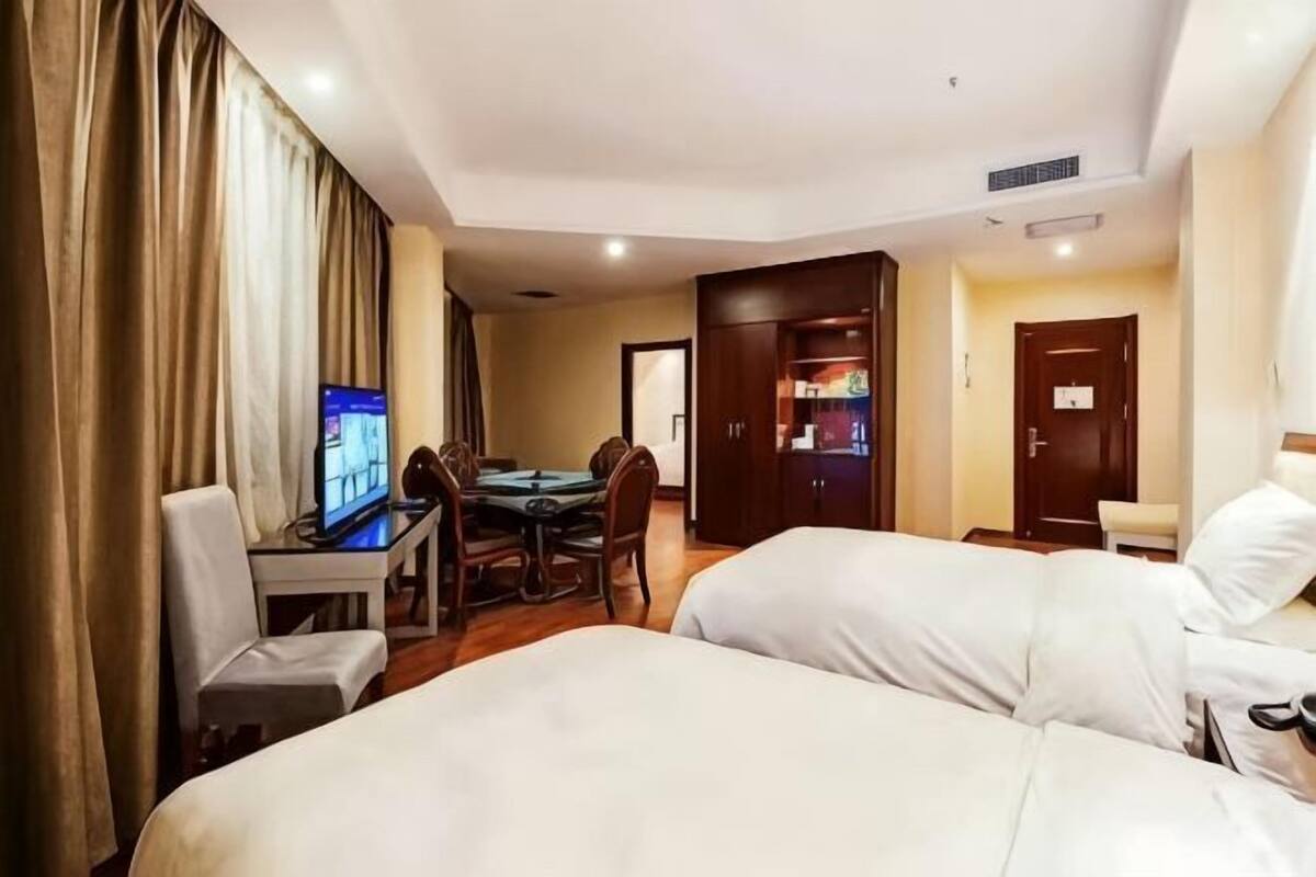 A hotel room with two beds, a desk with a chair, a television, a dining table, and a wardrobe.