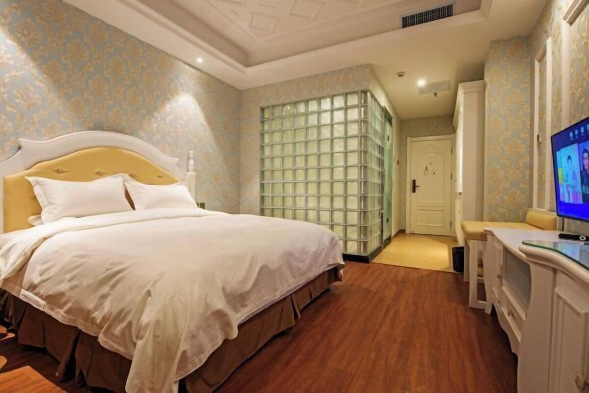 A hotel room with a large bed, a television, a desk, and a wardrobe.