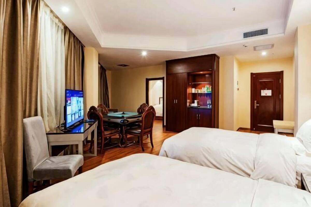 A hotel room with two beds, a dining table with chairs, a television, and a minibar.