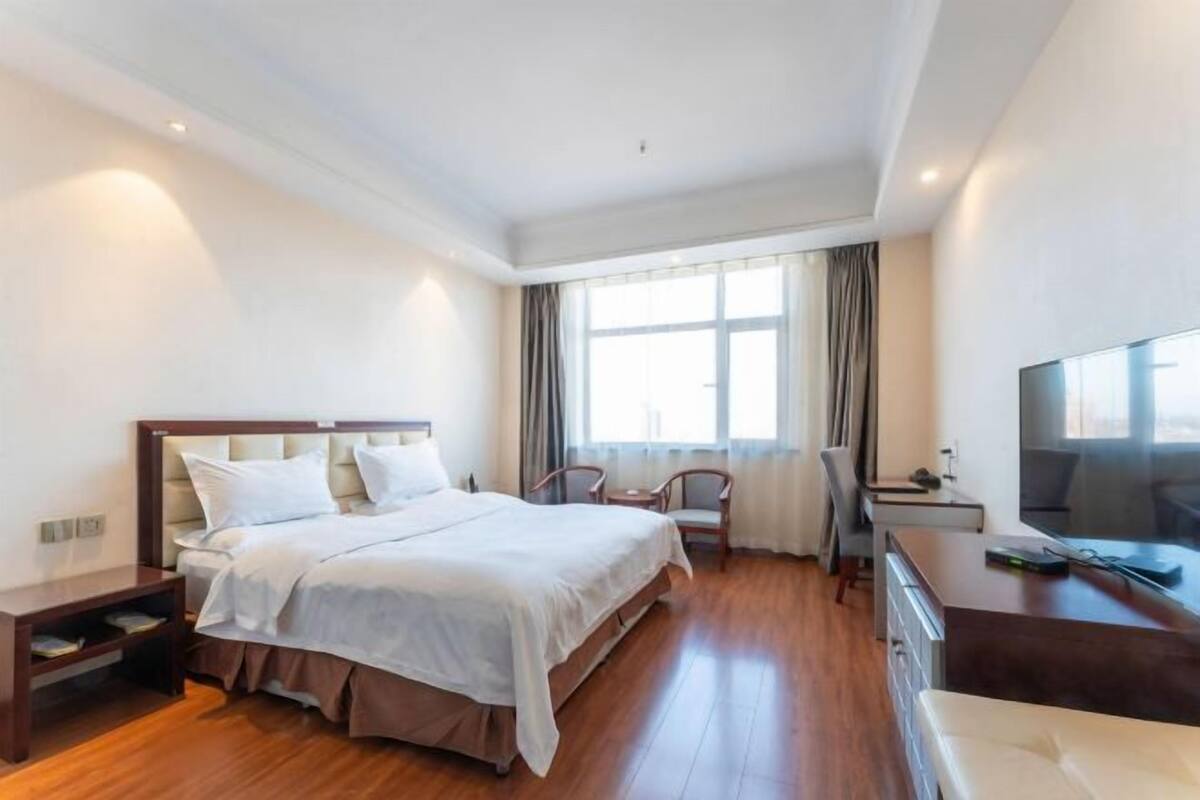 A hotel room with a large bed, a desk, a chair, a television, and a window with curtains.
