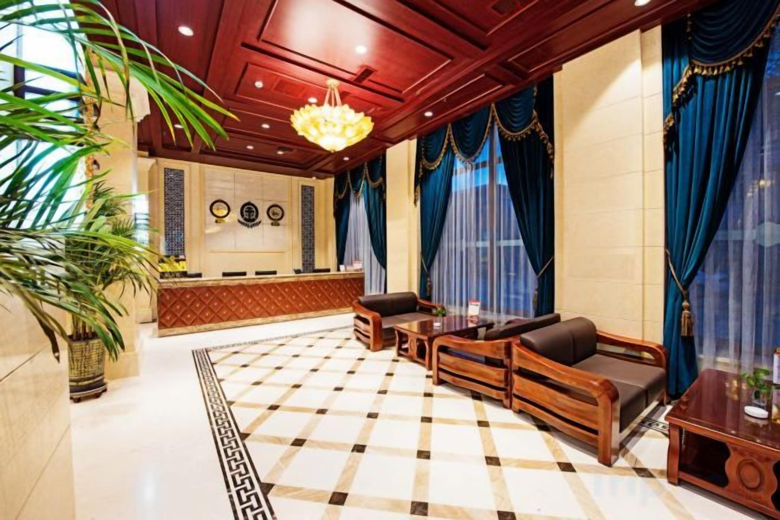 A lobby with a checkered floor, a reception desk, seating area with sofas and a coffee table, and a large chandelier.
