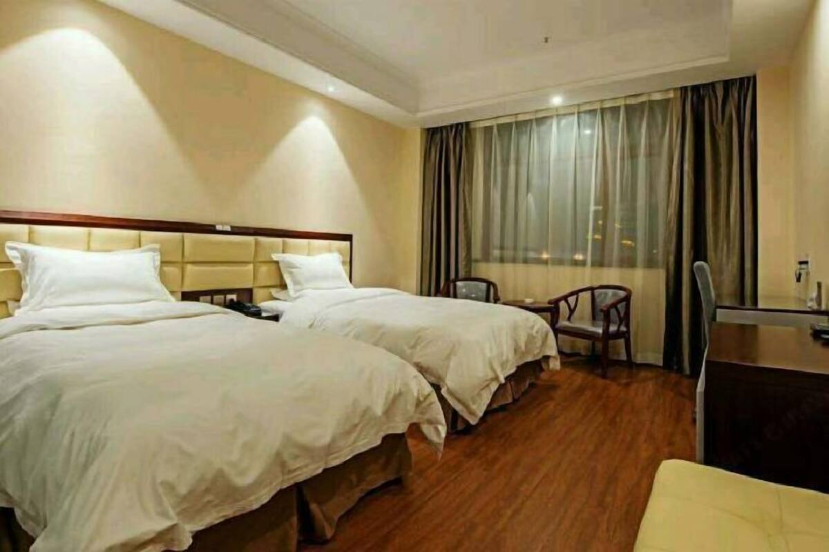 A hotel room with two beds, a desk, a chair, and a large window with curtains.