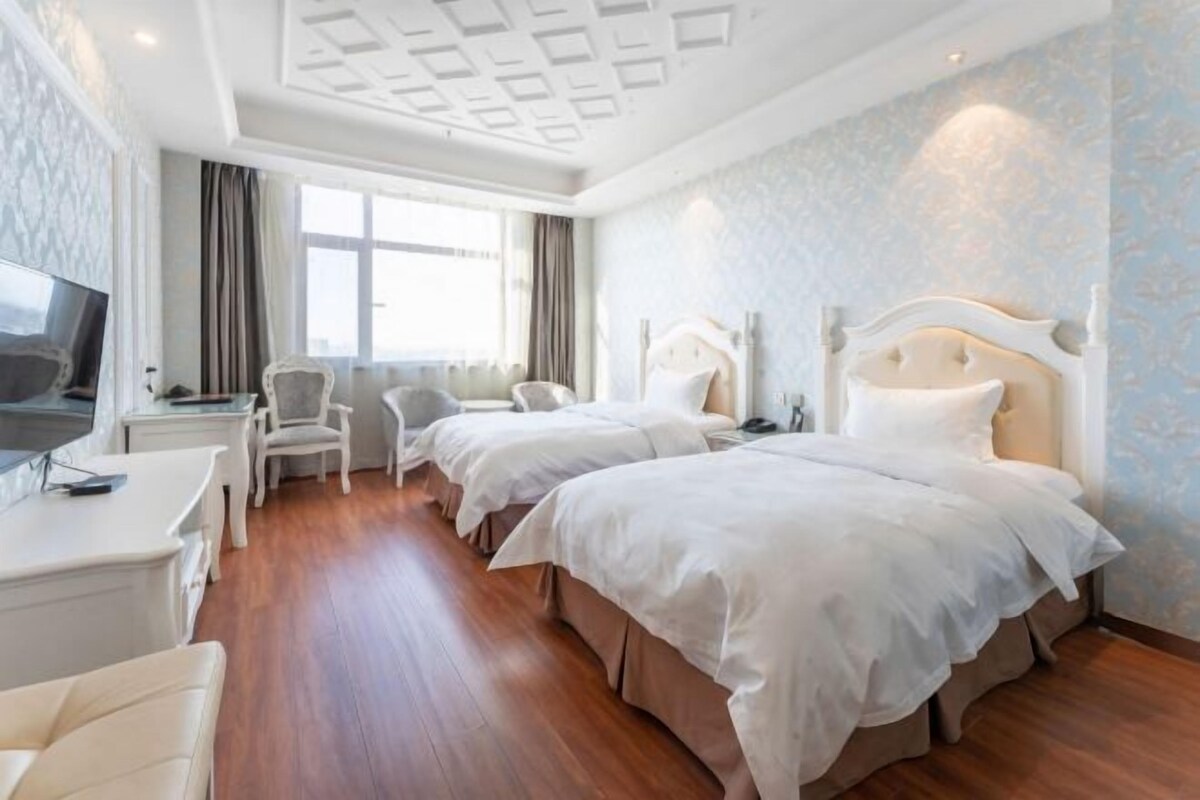 A hotel room with two beds, a desk, a chair, and a television.