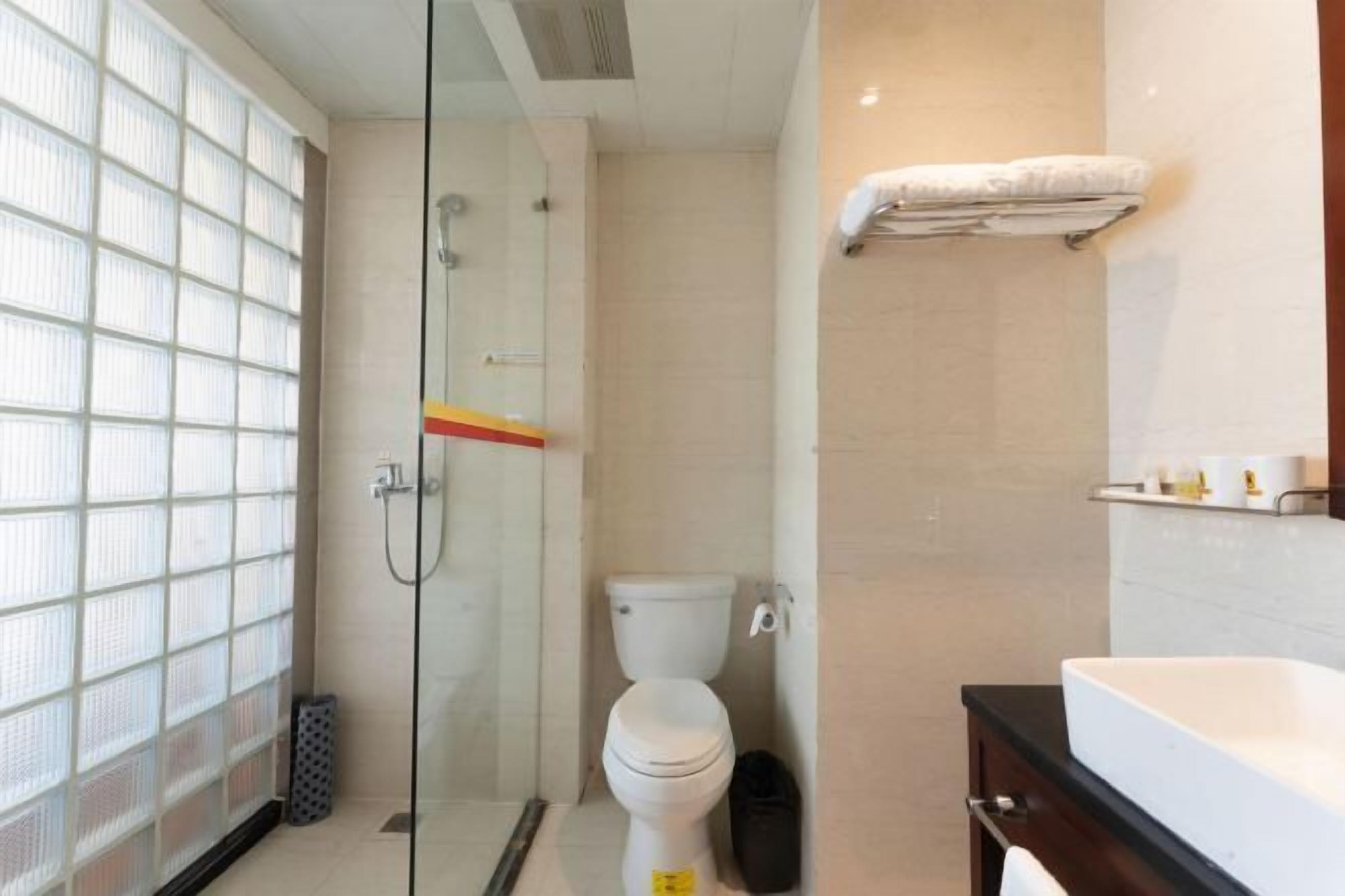 A bathroom with a glass shower enclosure, a toilet, a sink, and a towel rack.