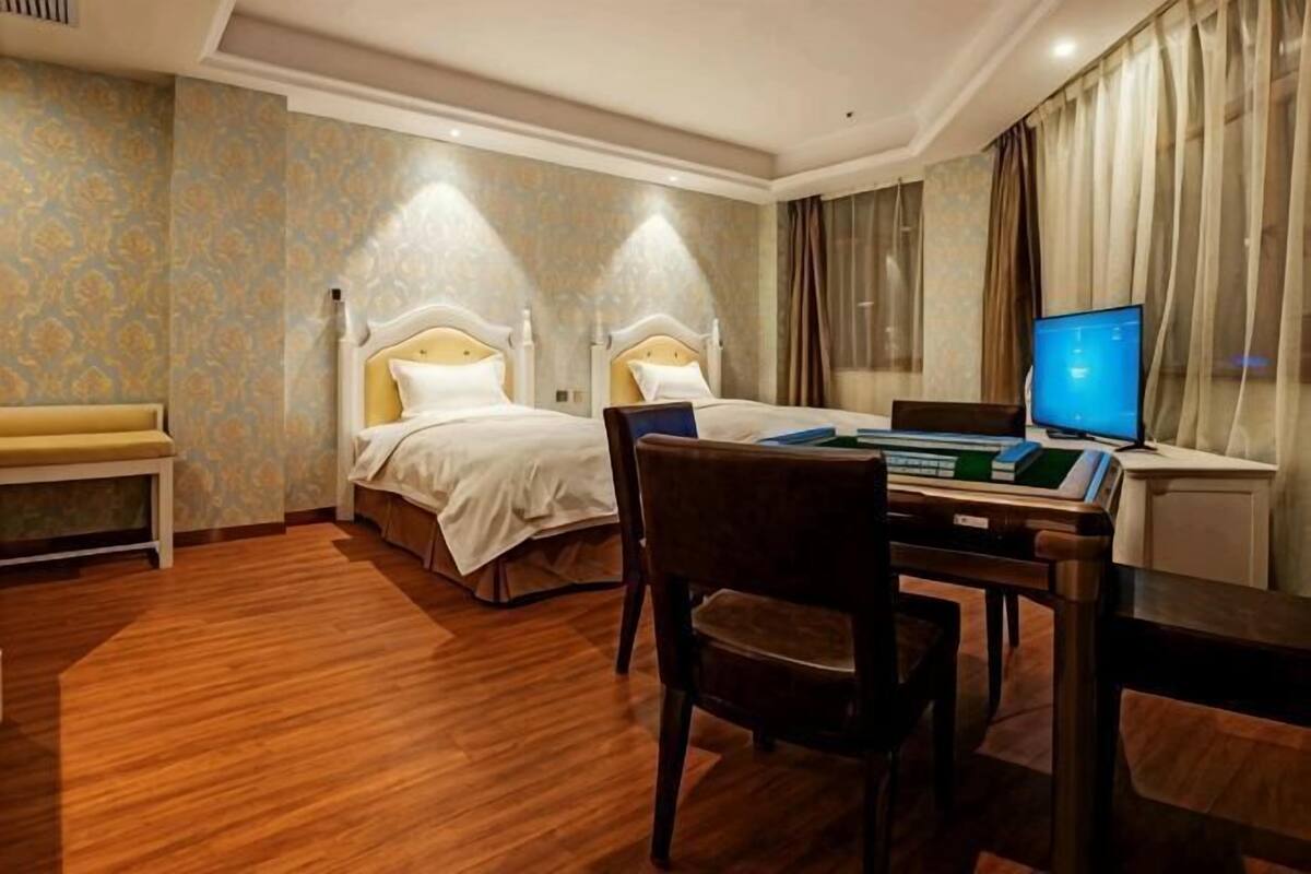 A hotel room with two beds, a desk with a laptop, a chair, and a bench.