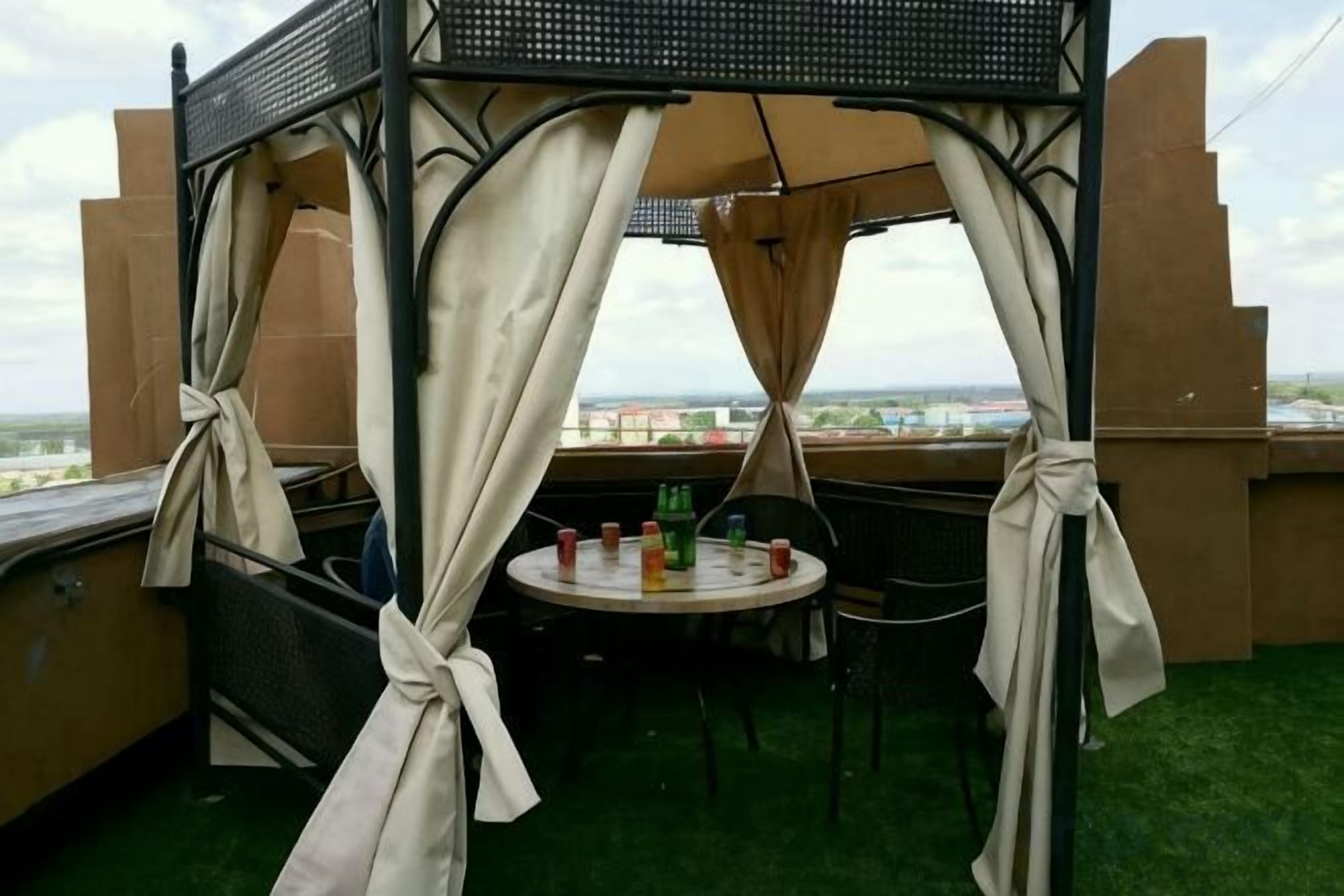 Ein überdachter Außenbereich mit Tisch und Stühlen, Blick auf die Stadtlandschaft und einem Belag aus grünem Kunstrasen.