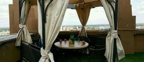 A covered outdoor seating area with a table and chairs, a view of the cityscape, and a green artificial turf floor.