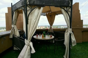 Un espacio al aire libre techado con mesa y sillas, vista panorámica de la ciudad y piso de césped artificial.