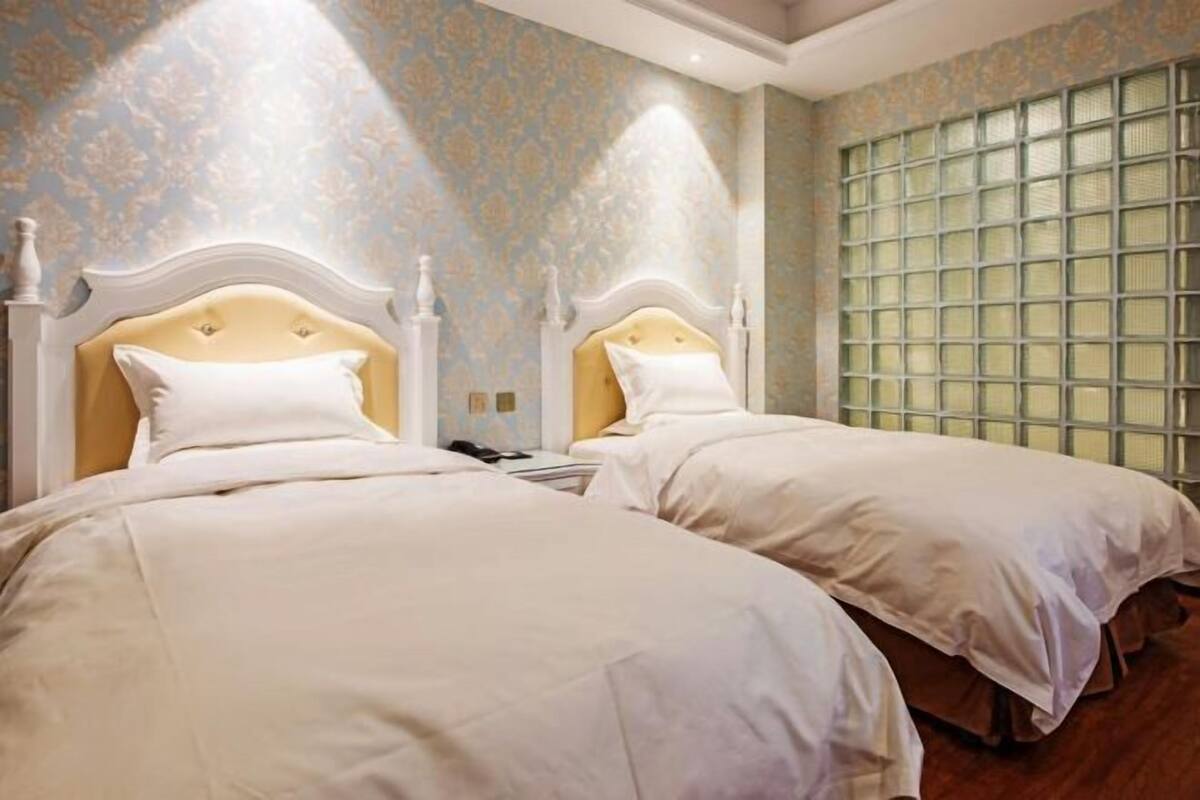 A hotel room with two beds, a large window with a grid pattern, and a patterned wallpaper.