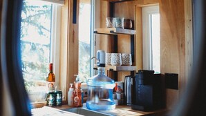 A kitchen with wooden cabinets, a coffee maker, and a water dispenser. - It is a tiny home in the treehouse located in the middle of Fairbanks. (Fairbanks)