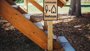 A wooden staircase leading to a covered area with a sign indicating a chickadee treehouse. - It is a tiny home in the treehouse located in the middle of Fairbanks. (Fairbanks)