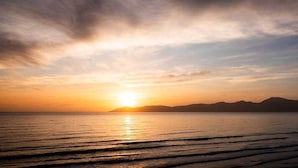 A sunset over a calm sea with distant mountains. - Seascapes Beach House (Paraparaumu)