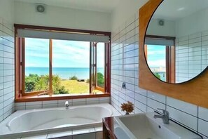 Une salle de bain dotée d’une grande baignoire, d’un lavabo et d’une fenêtre donnant sur l’océan.