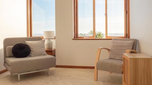 A room with a sofa, a chair, a small table, and a window with a view. - Seascapes Beach House (Paraparaumu)