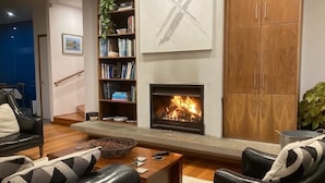 A living room with a fireplace, bookshelves, and leather furniture. - Seascapes Beach House (Paraparaumu)