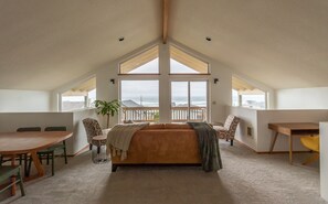 A spacious attic bedroom with a large bed, a dining table, and chairs. It features a view of the ocean through large windows. - Tranquil ocean view, walk to beach, king suite (Lincoln City)