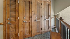 A set of wooden double doors with louvered panels and metal handles, leading to a staircase with a wooden handrail and a carpeted floor.