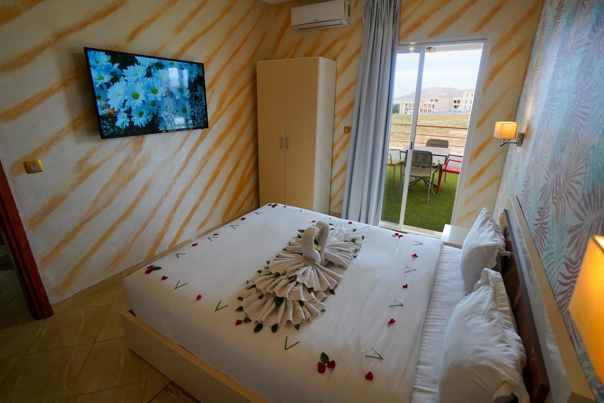 A hotel room with a bed, a television on the wall, a wardrobe, and a view of the outside.
