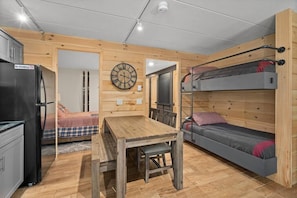 Une petite pièce comprenant un lit superposé, une table à manger, un réfrigérateur et une horloge murale.