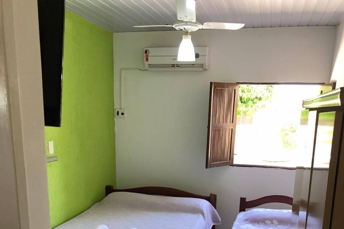 A small, clean room with two beds, a ceiling fan, an air conditioning unit, and a window with curtains.