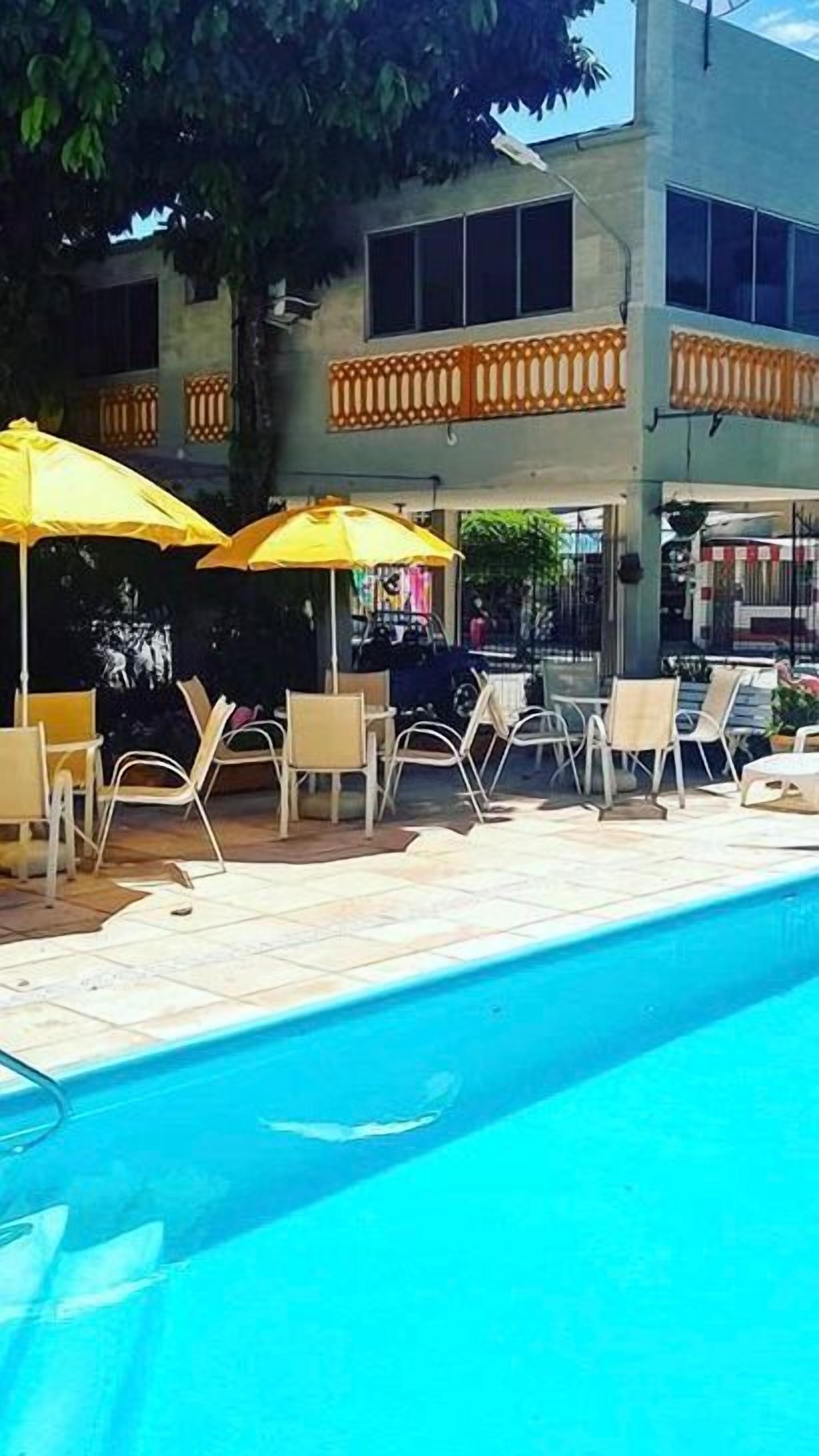 A pool area with lounge chairs and umbrellas, a building with balconies, and a clear blue pool.