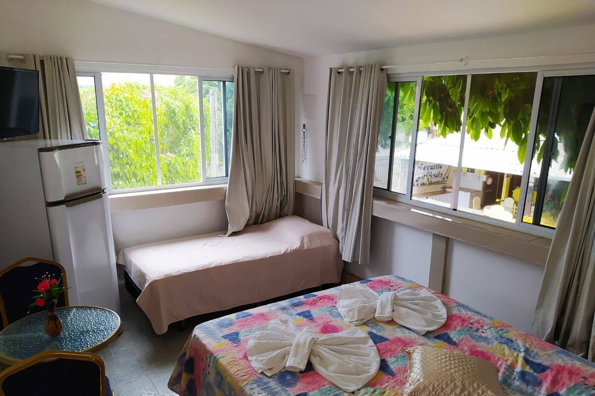 A hotel room with two beds, a small table with a vase, a television, and curtains.