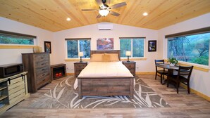 A bedroom with a wooden ceiling, a large bed, a fireplace, a dining area, and large windows with a view of trees. - Red Mountain Suite 1 mile to Sequoia Natl Park! (Three Rivers)