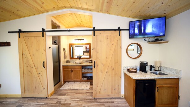 A kitchen with wooden cabinets, a black refrigerator, a sink, a coffee maker, and a television mounted above the counter. - Red Mountain Suite 1 mile to Sequoia Natl Park! (Three Rivers)