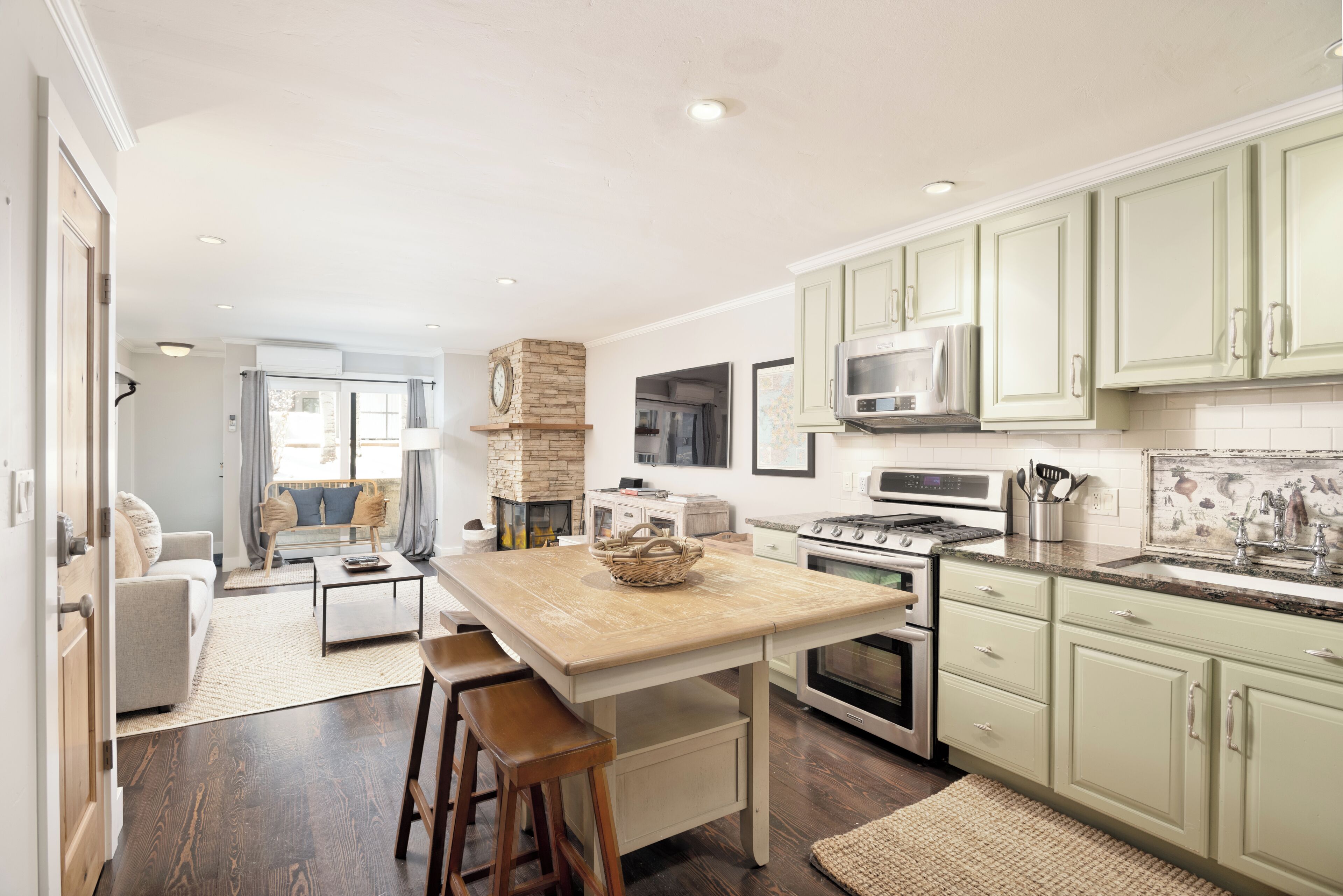 A modern kitchen with light green cabinets, a central island, and a dining area with a sofa and chairs.