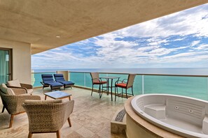 Ein Balkon mit Korbmöbeln, einem Tisch und einem Whirlpool mit Blick auf das türkisfarbene Meer.