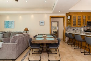 Ein modernes Wohnzimmer mit einer Couch und einem Esstisch mit Stühlen. Es gibt eine Küchenzeile mit Holzschränken und einer Arbeitsplatte.