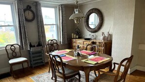 Een eetkamer met een houten tafel, stoelen, een vloerkleed, een kroonluchter, een spiegel en een raam met gordijnen.
