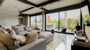 Una sala de estar moderna con un amplio sofá modular, un comedor con mesa y sillas, y ventanas grandes con vista a la ciudad.
