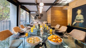 Un comedor con mesa de vidrio, sillas, productos para el desayuno y un cuadro en la pared.
