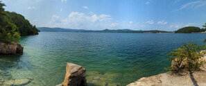 A clear view of a lake with a rocky shoreline and distant mountains. - The Jocassee Tiny House (Salem)