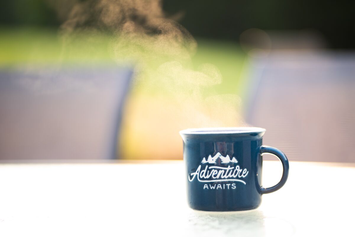 Une tasse bleue sur laquelle est inscrit le texte « L’aventure vous attend » est posée sur une table.
