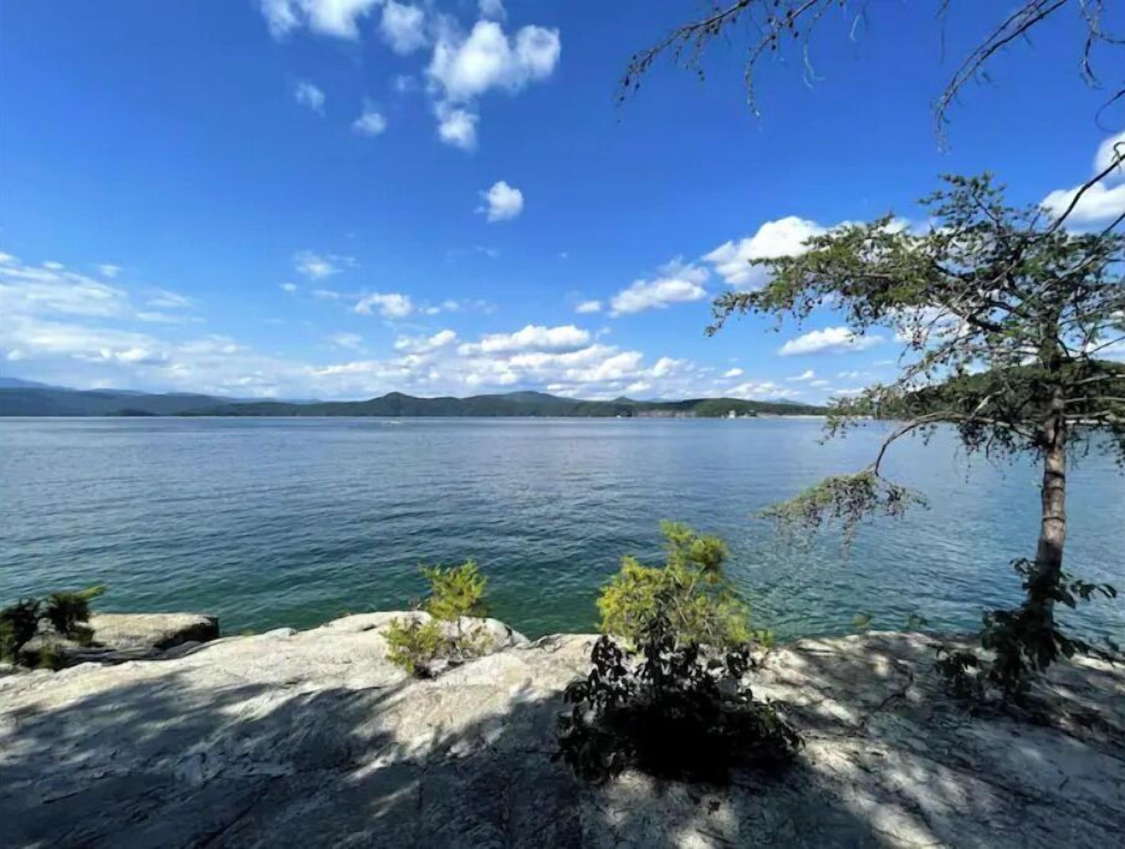 Um lago calmo sob um céu claro, com montanhas ao longe.