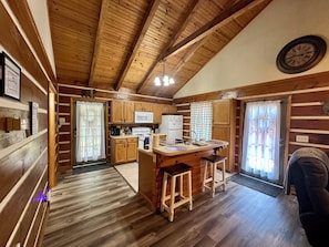 A wooden cabin interior with a kitchen, wooden floors, and a clock on the wall.