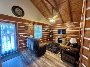 A log cabin interior with a ceiling fan, a television, a fireplace, and a couch.