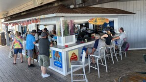 A beachside food kiosk with a menu board, a beer advertisement, and a bar area with stools. - Sand In My Boots<br>Condo Beach view, 3 bed, 1 bath (Murrells Inlet)