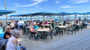 An outdoor dining area with tables and chairs under blue umbrellas, overlooking a beach. - Sand In My Boots<br>Condo Beach view, 3 bed, 1 bath (Murrells Inlet)