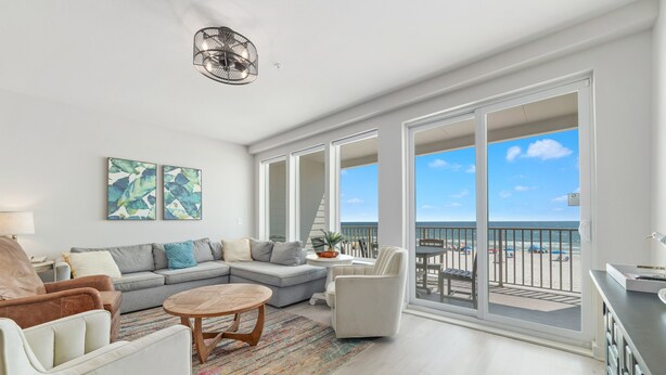 Een ruime woonkamer met een grijze modulaire bank, een bijzettafeltje en uitzicht op het strand door grote schuifdeuren.