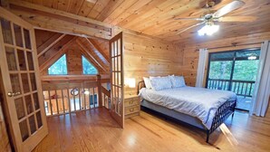A wooden cabin bedroom with a bed, a window, and a ceiling fan. - Wolf`s Den - Dogs OK- Hot Tub-Firepit-Wi-Fi-Fireplace-Covered Deck with Gas Grill (Blue Ridge)