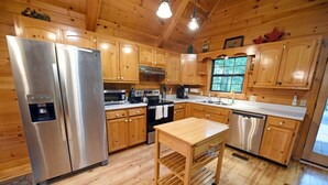 A modern kitchen with wooden cabinets, stainless steel appliances, and a central island. - Wolf`s Den - Dogs OK- Hot Tub-Firepit-Wi-Fi-Fireplace-Covered Deck with Gas Grill (Blue Ridge)