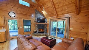 A log cabin interior with a stone fireplace, leather sofa, and a television. - Wolf`s Den - Dogs OK- Hot Tub-Firepit-Wi-Fi-Fireplace-Covered Deck with Gas Grill (Blue Ridge)