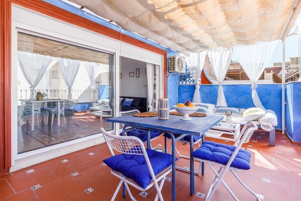 Un área de comedor al aire libre con una mesa, sillas y una sombrilla azul.