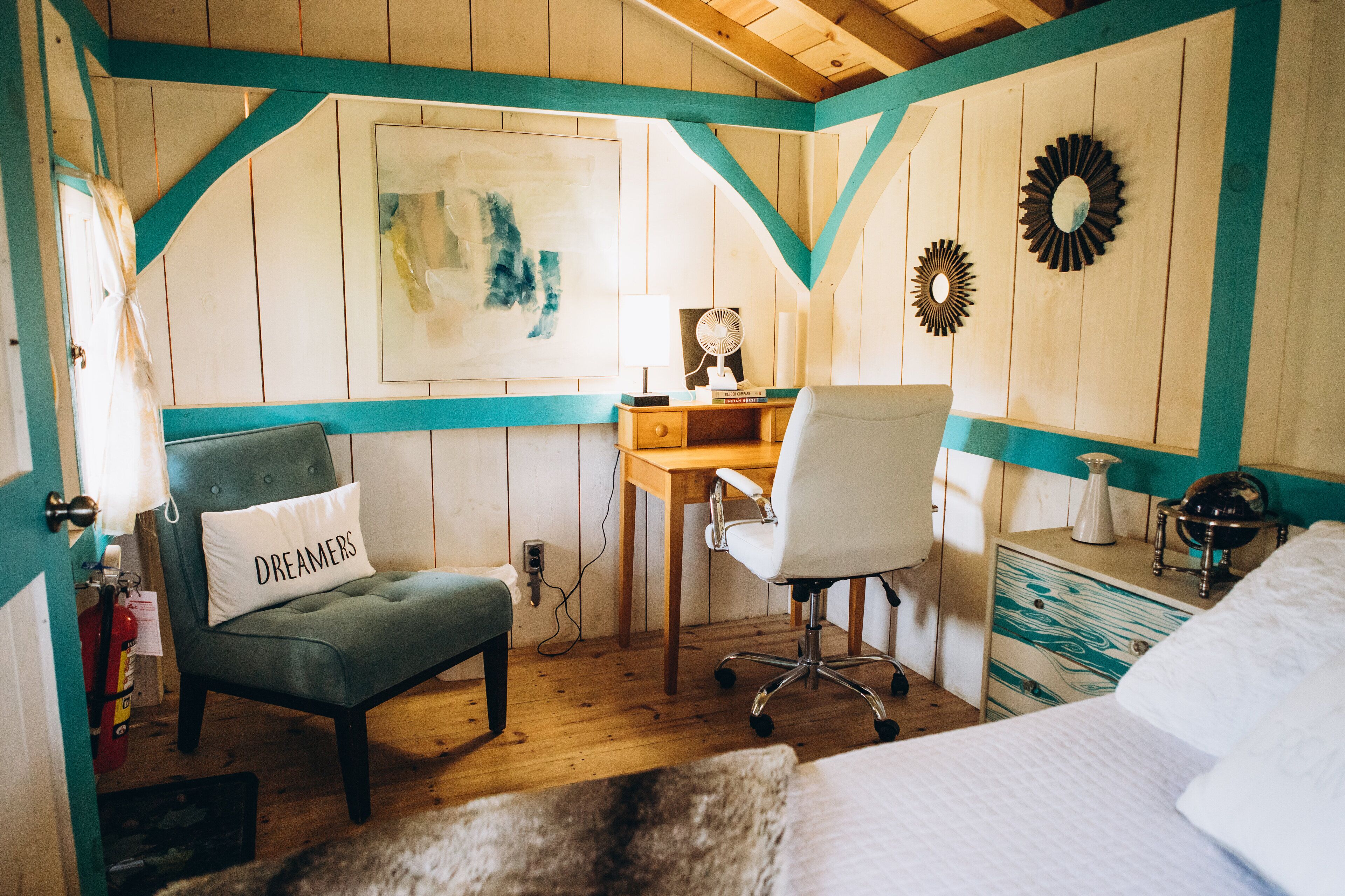 A cozy bedroom with a green armchair, a white bed, a wooden desk, and a chair.