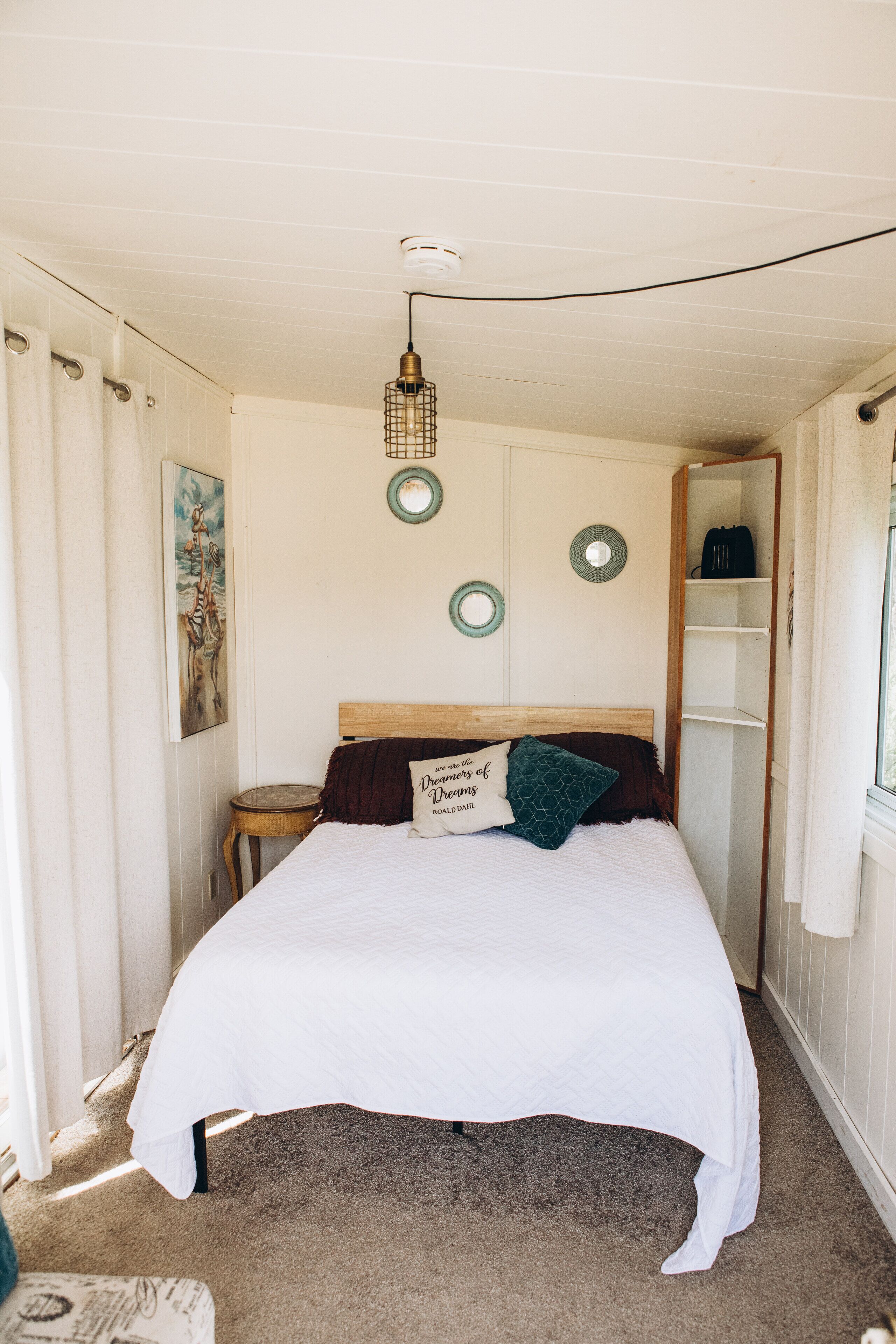 A bedroom with a bed, a nightstand, a shelf, and a hanging light fixture.